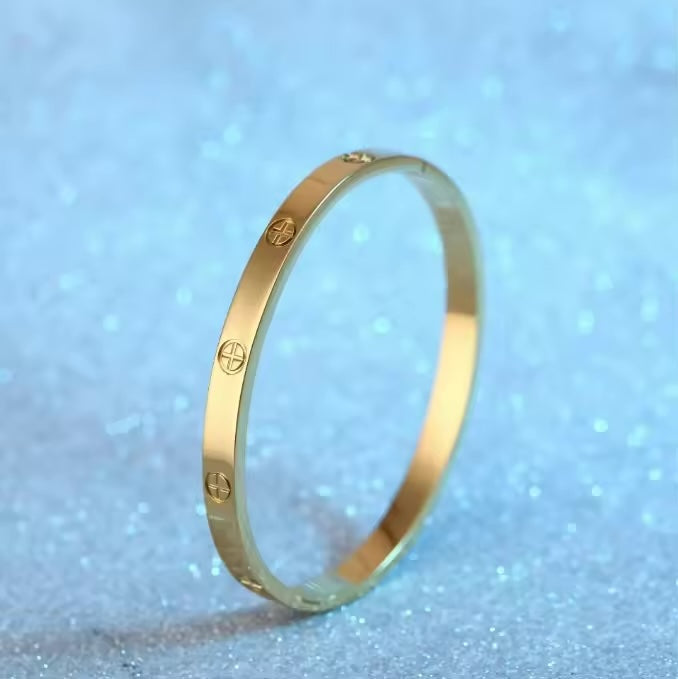 Goldfarbener Armreif mit Schraubenoptik aus Edelstahl auf hellem Untergrund
